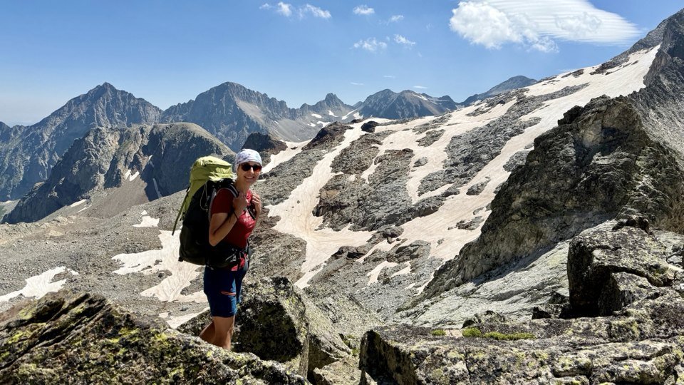 Martina mit Rucksack auf einem Grat vor schneebedeckten Berggipfeln